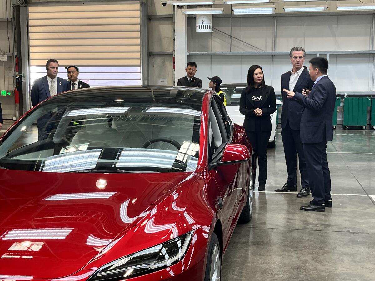 Gov. Gavin Newsom stands next to a red Tesla.
